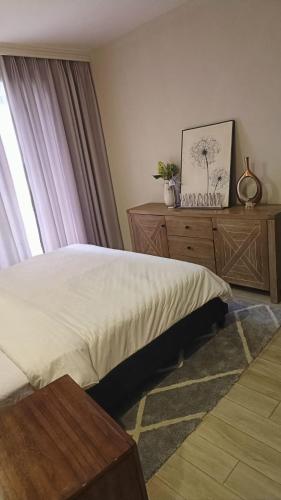 a bedroom with a bed and a dresser and a window at InDesign Makumbi Park Apartments near 67 airport hotel in Syokimau
