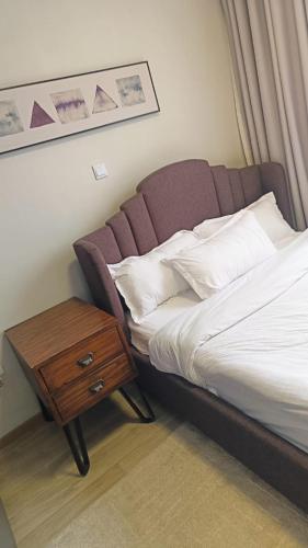 a bed with a wooden night stand next to a table at InDesign Makumbi Park Apartments near 67 airport hotel in Syokimau