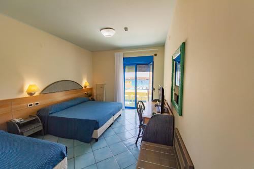 a bedroom with a bed and a desk with a television at Hotel Baia Turchese in Lampedusa