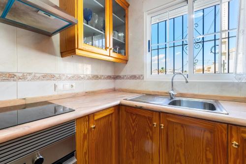 een keuken met houten kasten, een wastafel en een raam bij AZUL by the Sea in Villamartin