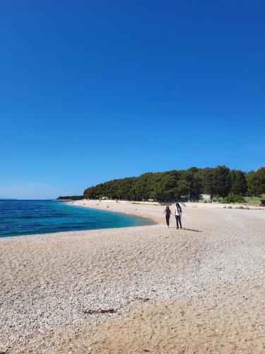 two people walking on a beach near the water at Apartment TRI MASLINE with seaview in Trogir