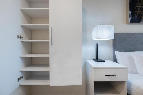 a white bedroom with a lamp on a night stand at Soka Suites Dallas - Las Colinas in Irving