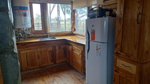 La cuisine est équipée d'un réfrigérateur blanc et de placards en bois. dans l'établissement Cabaña La Fortaleza Villa Yacanto, à Villa Yacanto