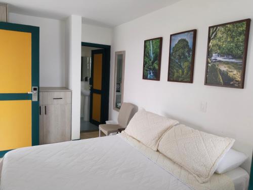 a bedroom with a white bed and three pictures on the wall at Colina del Sol Hotel Hacienda in Quimbaya