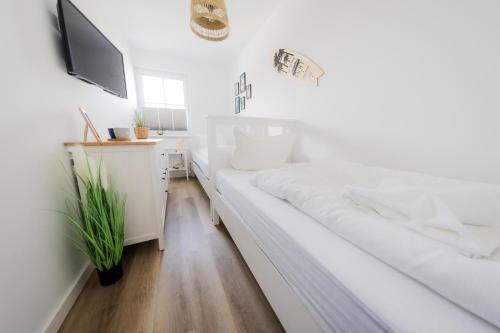 a white bedroom with a white bed and a tv at Haus Q Superior - Hälfte 2 in Zingst