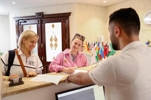 un hombre parado en un mostrador hablando con dos mujeres en Nemi Hotel Baku en Bakú