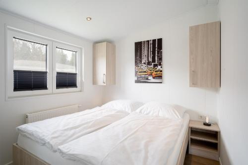 a white bedroom with a bed and two windows at Ostseecamp Chalet Haffkrug No 59 in Scharbeutz