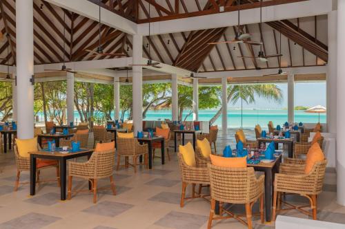 a restaurant with tables and chairs and the ocean at Cinnamon Dhonveli Maldives in North Male Atoll