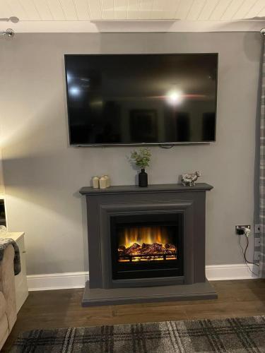 a living room with a fireplace with a television above it at Riverbank Lodge in Dollar