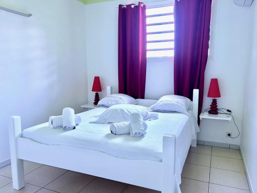 un letto bianco in una camera da letto con tende viola di Bleu Soleil a Le Morne-Vert