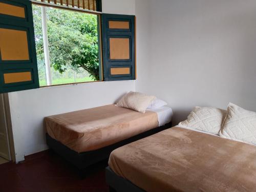 two beds in a room with a window at Colina del Sol Hotel Hacienda in Quimbaya