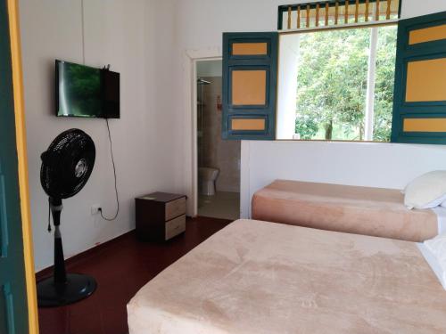a room with two beds and a fan and a window at Colina del Sol Hotel Hacienda in Quimbaya