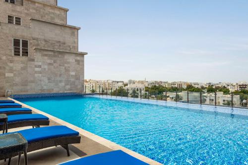 a large swimming pool with chairs and a building at Radisson Hotel Muscat Panorama in Muscat