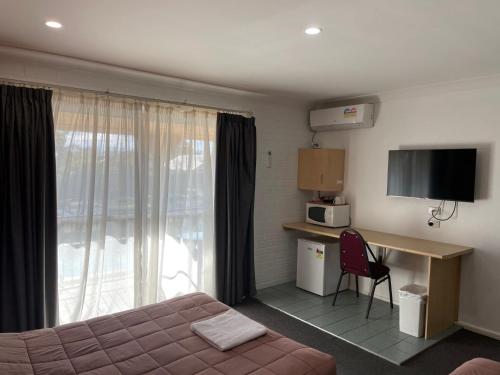a hotel room with a bed and a desk and a window at Homestead Motel in Dubbo