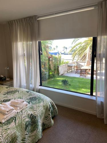 Schlafzimmer mit einem großen Fenster mit Blick auf den Hof in der Unterkunft Palm Garden Apartment in Auckland
