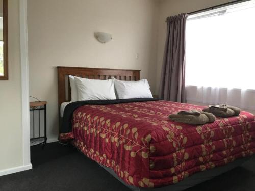 a bedroom with a bed with a red blanket and a window at Aaron Court Motel in Timaru