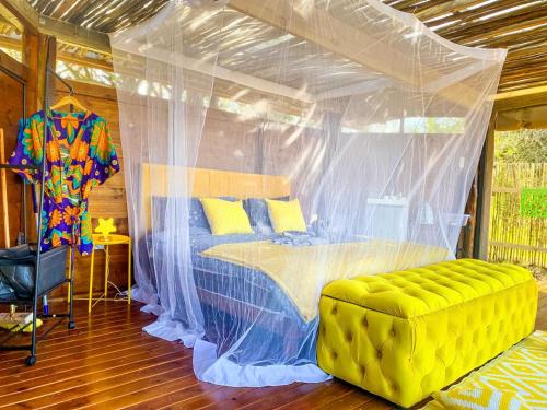 シュルシュルウェにあるHluhluwe Bush Camp Glamping Villageのベッドルーム(天蓋付きベッド1台、黄色いソファ付)