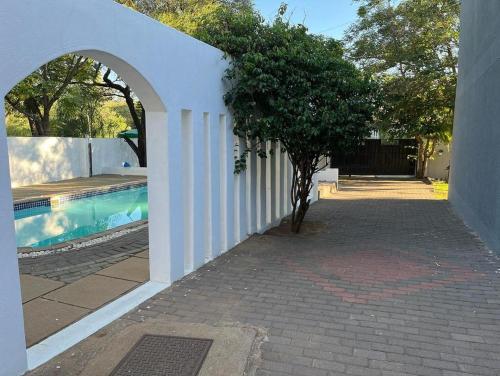a white wall with a tree next to a swimming pool at Shiloh Inn in Gaborone