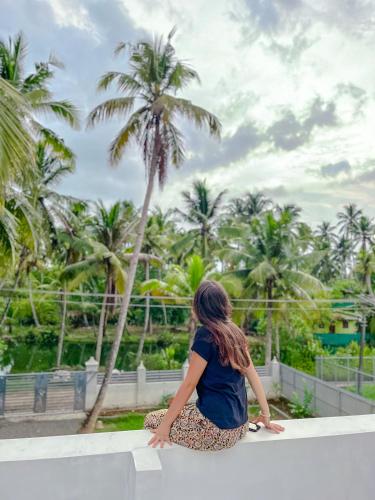 a woman sitting on a ledge looking at palm trees at Riverrootsstays in Munroe Island