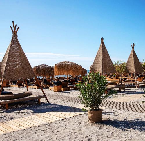 a beach with chairs and straw umbrellas and tables at Azul Sunrise in Mamaia Sat/Năvodari