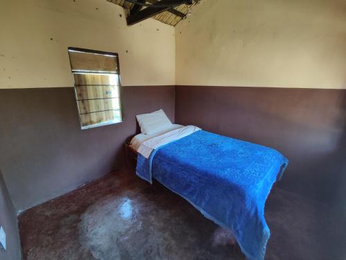 a bedroom with a bed with a blue blanket and a window at Simoonga Thandizani School in Livingstone