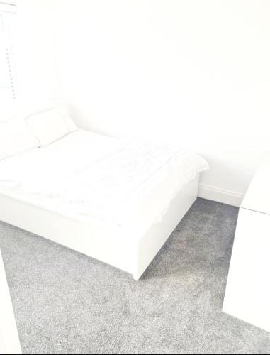 Una cama blanca en una habitación blanca con en 3 Bedroom House London, en Harrow