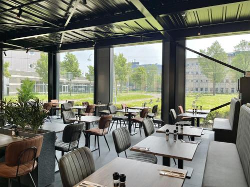 un ristorante con tavoli, sedie e ampie finestre di OZO Hotels Antares Airport a Hoofddorp