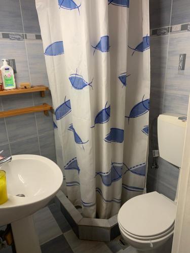 a bathroom with a toilet and a shower curtain with fish on it at The Light Blue House in Karavostamo