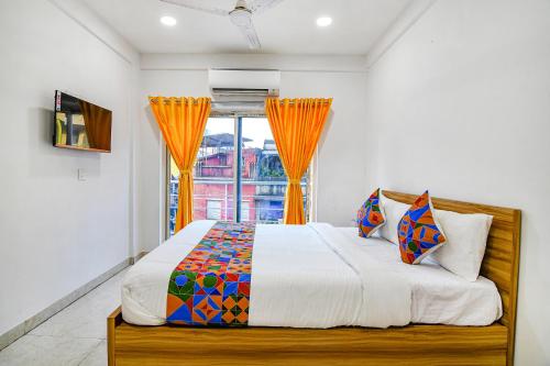 a bedroom with a bed and a window with orange curtains at FabHotel Grand Hazra Inn - Nr Ballygunge Station in Kolkata