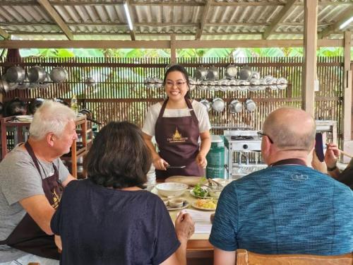 Eine Gruppe von Menschen, die in einer Küche um eine Frau stehen in der Unterkunft The Thai House Homestay & Thai Cooking Experiences in Ban Bang Sano