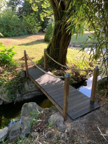 un pont en bois sur un ruisseau avec un arbre dans l'établissement La petite maison de la gare, à Nemours