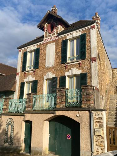 un antiguo edificio de ladrillo con una puerta verde y un balcón en Les Logis Aux portes de la Vallée de Chevreuse, 