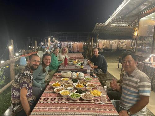 un gruppo di persone seduti intorno a un tavolo con cibo di Bao Lac Homestay Hostel & Coffee a Bảo Lạc