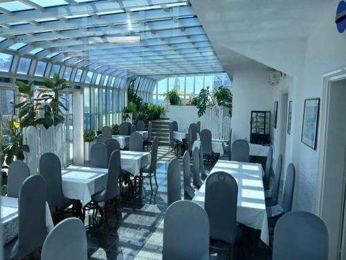 un restaurante con mesas blancas, sillas y plantas en Hotel Biser en Pag