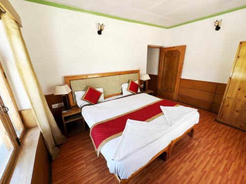 a bedroom with a large bed with white sheets and red pillows at Hotel Lumbini in Leh