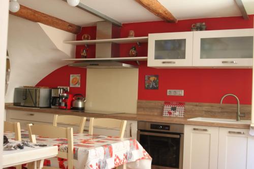 une cuisine avec des murs rouges, des armoires blanches et une table dans l'établissement Lourecantou, à Saint-Thibéry