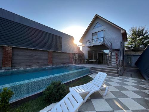 a swimming pool with two white chairs next to a house at Qafqaz Suite Paradise Chalet & SPA in Gabala
