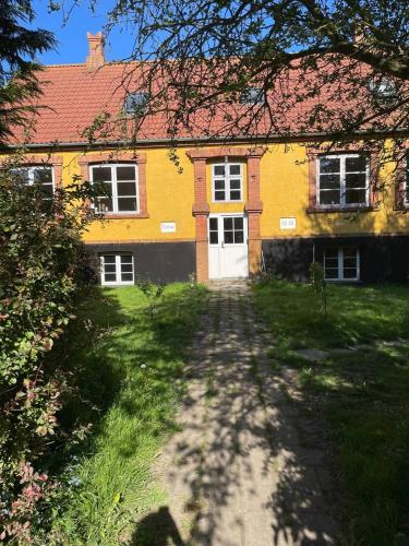 a yellow house with a white door and a yard at Homestay in charming house on the countryside in Rønne