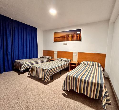 two beds in a room with blue curtains at Pension La Orozca in Benidorm