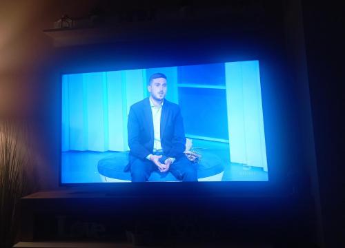 Un uomo in giacca e cravatta seduto su una sedia sullo schermo della televisione. di CASA VACANZA LA MANSARDINA a Pavia