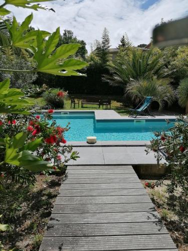 a swimming pool with a wooden walkway in a garden at Via Bahia - Maison d'hôtes in Biscarrosse