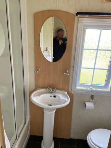 Ein Mann fotografiert ein Badezimmer mit Waschbecken. in der Unterkunft Pen llyn holiday cottages and caravan in Newborough