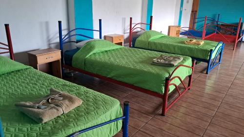 a room with three beds with green sheets and a table at Hostal Dulces Sueños in Panajachel