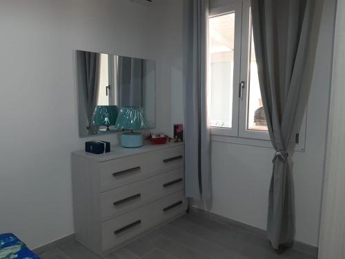 - une commode blanche avec un miroir et une fenêtre dans l'établissement SARDEGNA VACANZE BIVANo MARCO, à Flumini di Quartu