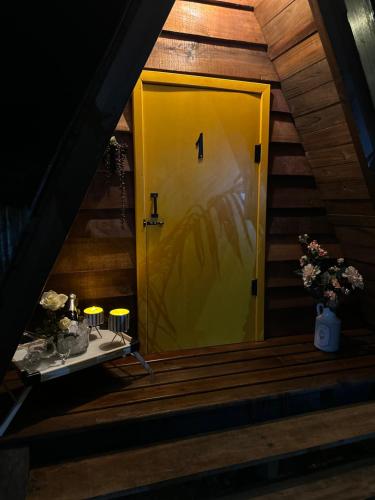 uma porta amarela numa escada com flores e velas em Glamping casal - mini chale mobiliado com colchão casal roupa de cama travesseiros - Rancho Perene estação rural em Jaraguá do Sul