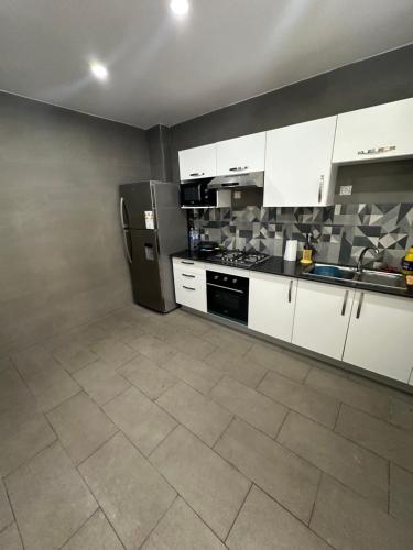 La cuisine est équipée de placards blancs et d'un réfrigérateur noir. dans l'établissement Appartement reaprom, à Mostaganem