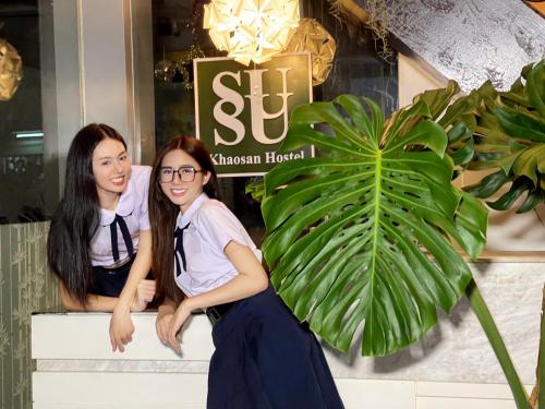dos chicas sentadas en un banco frente a una tienda en SUSU khaosan hostel, en Bangkok