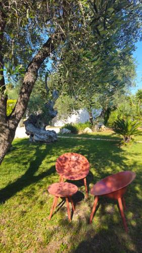 two tables and stools in the grass under a tree at Giardino Don Berardino in Mattinata