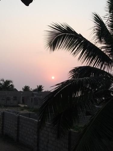 una puesta de sol detrás de una valla y una palmera en Akomapa Village, en Elmina