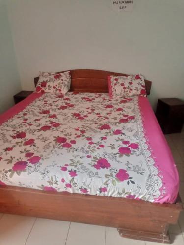 ein Bett mit einer rosa und weißen Bettdecke mit Blumen in der Unterkunft Résidence la Grâce Benkadi in Bobo-Dioulasso